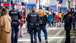 Zwei Polizisten laufen über den Stuttgarter Hauptbahnhof. Um sie herum stehen viele Menschen.