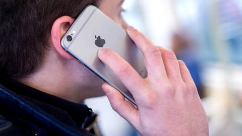 Ein junger Mann hält ein Smartphone der Marke Apple an sein Ohr.