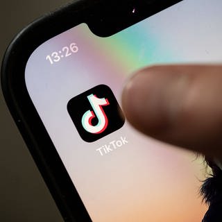 Ein Teenager tippt auf das Icon TikTok-App auf einem Smartphone.