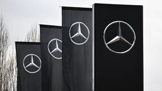 Das Logo der Automarke Mercedes-Benz weht an Fahnen vor einer Mercedes-Benz Niederlassung in Stuttgart.