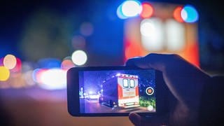 Auf einem Handy-Display sieht man einen Krankenwagen bei Nacht. Symbolbild für Gaffer an Unfallort.