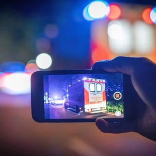 Auf einem Handy-Display sieht man einen Krankenwagen bei Nacht. Symbolbild für Gaffer an Unfallort.