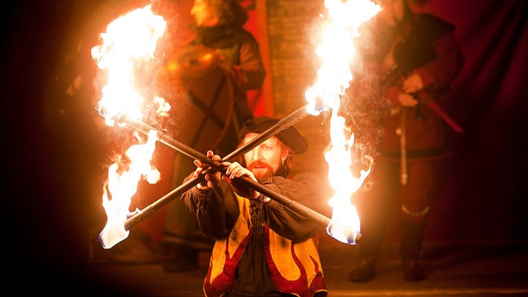Ein mittelalterlich gekleideter Akrobat jongliert mit zwei brennenden Fackeln
