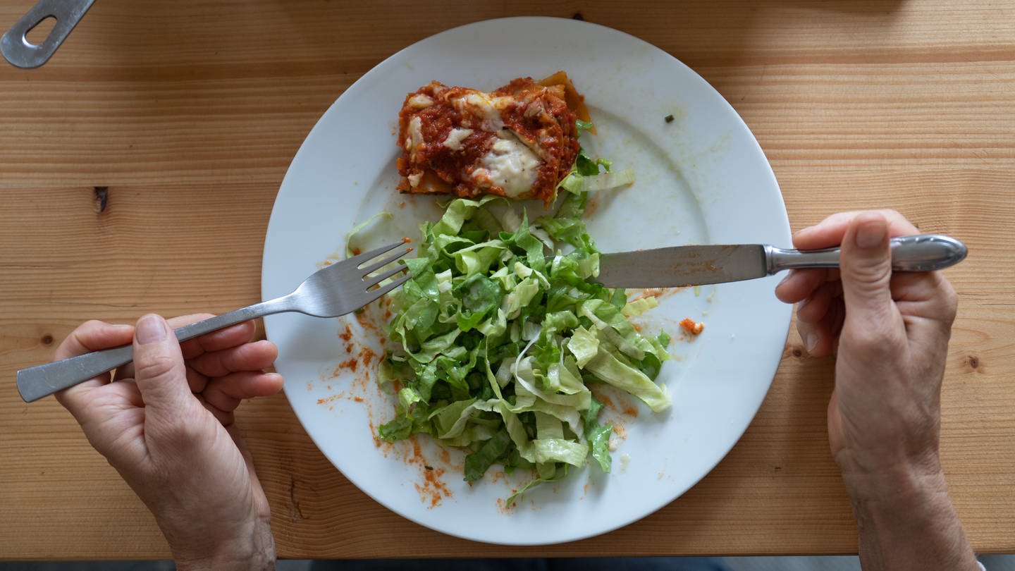 Eine Frau isst eine vegetarische Lasagne aus Linsen mit einem grünen Salat. Immer mittwochs gibt es in den Einrichtungen der Evangelischen Heimstiftung kein Fleisch mehr auf den Speiseplänen. Daran gibt es Kritik.