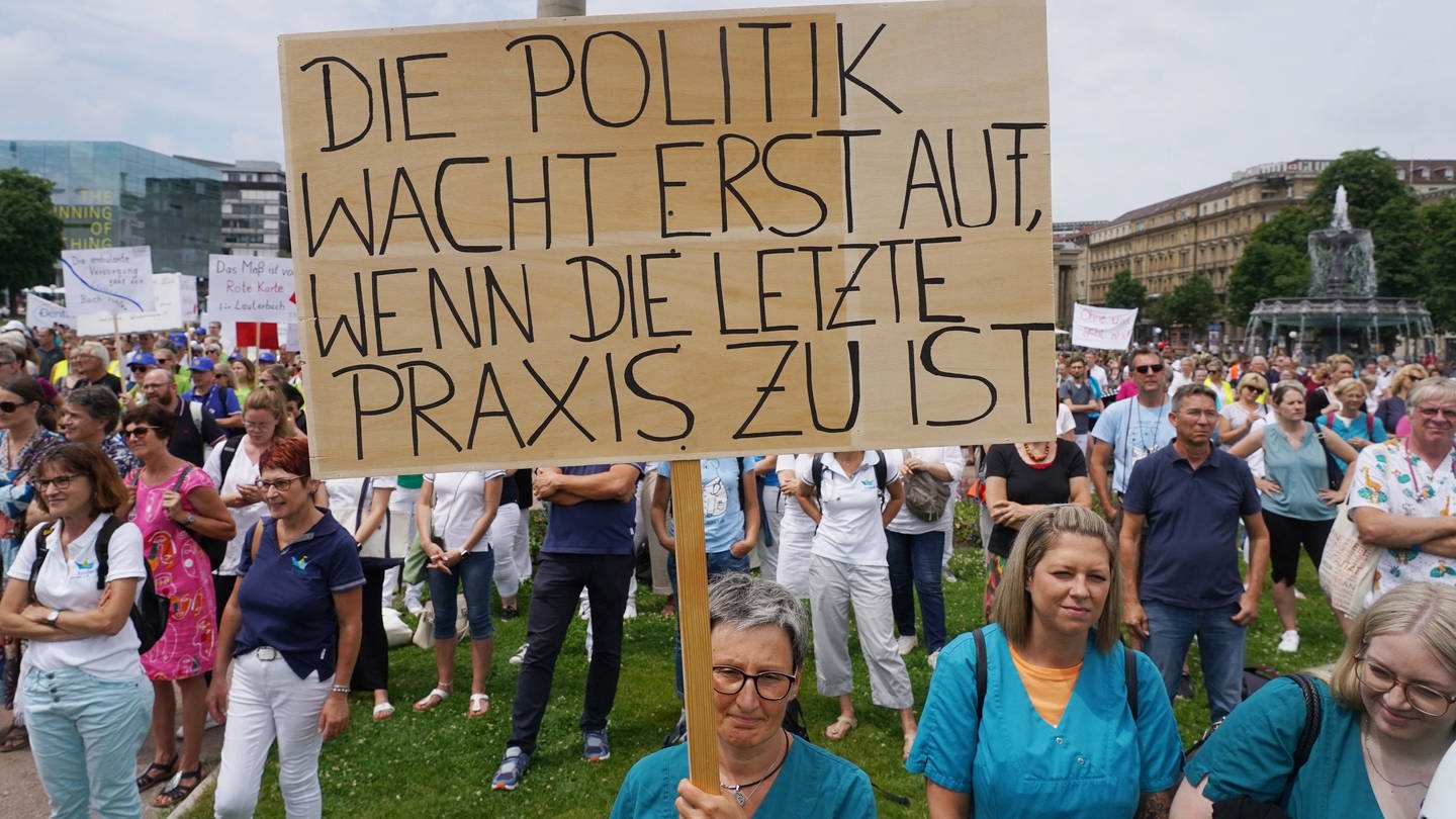 Niedergelassene Ärzte, Psychotherapeuten und Beschäftigte von Arztpraxen demonstrieren auf dem Schlossplatz in Stuttgart. Eine Teilnehmerin hält ein Schild hoch mit der Aufschrift: 