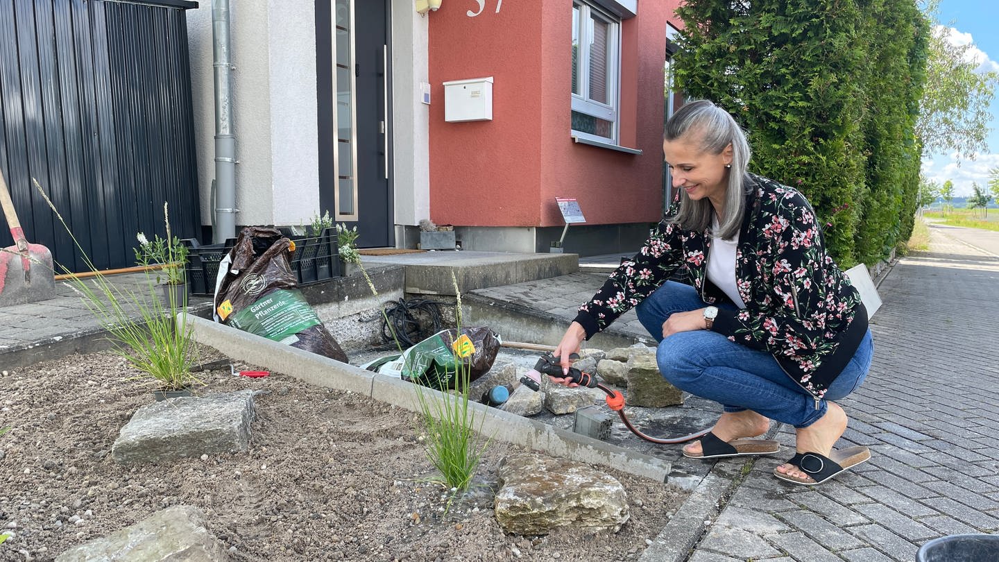 Eine Frau kniet vor ihrem neu gestalteten Vorgarten und gießt eine Pflanze
