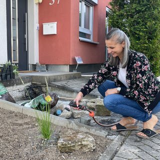Eine Frau kniet vor ihrem neu gestalteten Vorgarten und gießt eine Pflanze