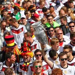 Deutsche Fans in weißen Trickots und mit Fahnen laufen im Pulk zusammen zu einem EM-Spiel (Archiv).