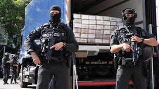 Vermummte und schwer bewaffnete Polizisten des LKA Baden-Württemberg bewachen in Stuttgart einen Lastwagen, in dem palettenweise Kokain lagert. Ermittler haben durch einen Coup 35,5 Tonnen der Droge beschlagnahmen können.