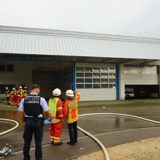 Feuerwehrleute und ein Polizist stehen bei einem Feuerwehreinsatz vor einer Werkstatt in Geislingen an der Steige (Kreis Göppingen). 