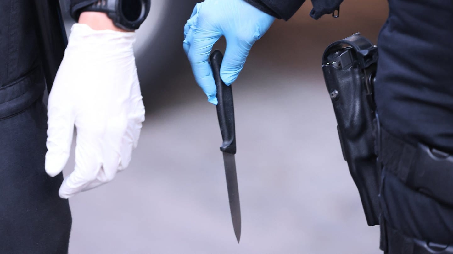 Zwei Polizisten, die beide Handschuhe haben. Einer der beiden trägt ein Messer in der Hand mit der spitzen Seite nach unten.