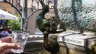 Am Hans-Im-Glück-Trinkwasserbrunnen in der Stuttgarter Innenstadt wird ein Glas Wasser mit Trinkwasser gefüllt.