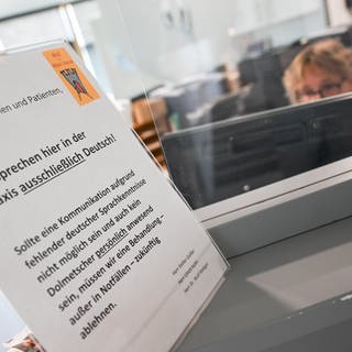 Ein Schild mit der Aufschrift "Wir sprechen hier in der Praxis ausschließlich Deutsch" steht auf einem Tresen an dem Empfangsbereich einer Praxis für Kinder- und Jugendmedizin in Kirchheim unter Teck.