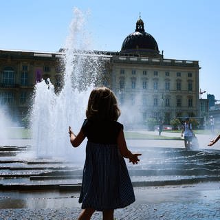 Bei wolkenlosem Himmel und sommerlichen Temperaturen am Lustgarten spielen Kinder am Brunnen.