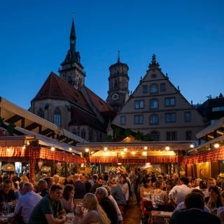 Menschen sitzen auf dem Stuttgarter Weindorf zusammen, trinken Wein und essen schwäbische Spezialitäten. 