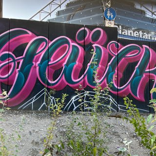 Das Graffiti mit dem Schriftzug "Glück" auf der Absperrung zwischen dem Stuttgart Planetarium und der U-Bahn-Haltestelle.