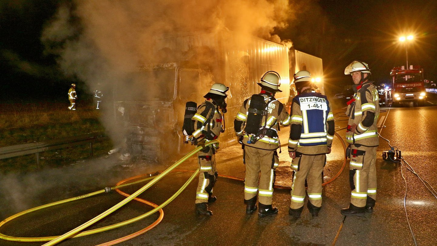 Feuerwehrleute löschen nachts einen brennenden Paketlaster auf der A81.