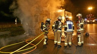 Feuerwehrleute löschen nachts einen brennenden Paketlaster auf der A81.