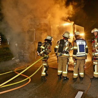 Feuerwehrleute löschen nachts einen brennenden Paketlaster auf der A81.