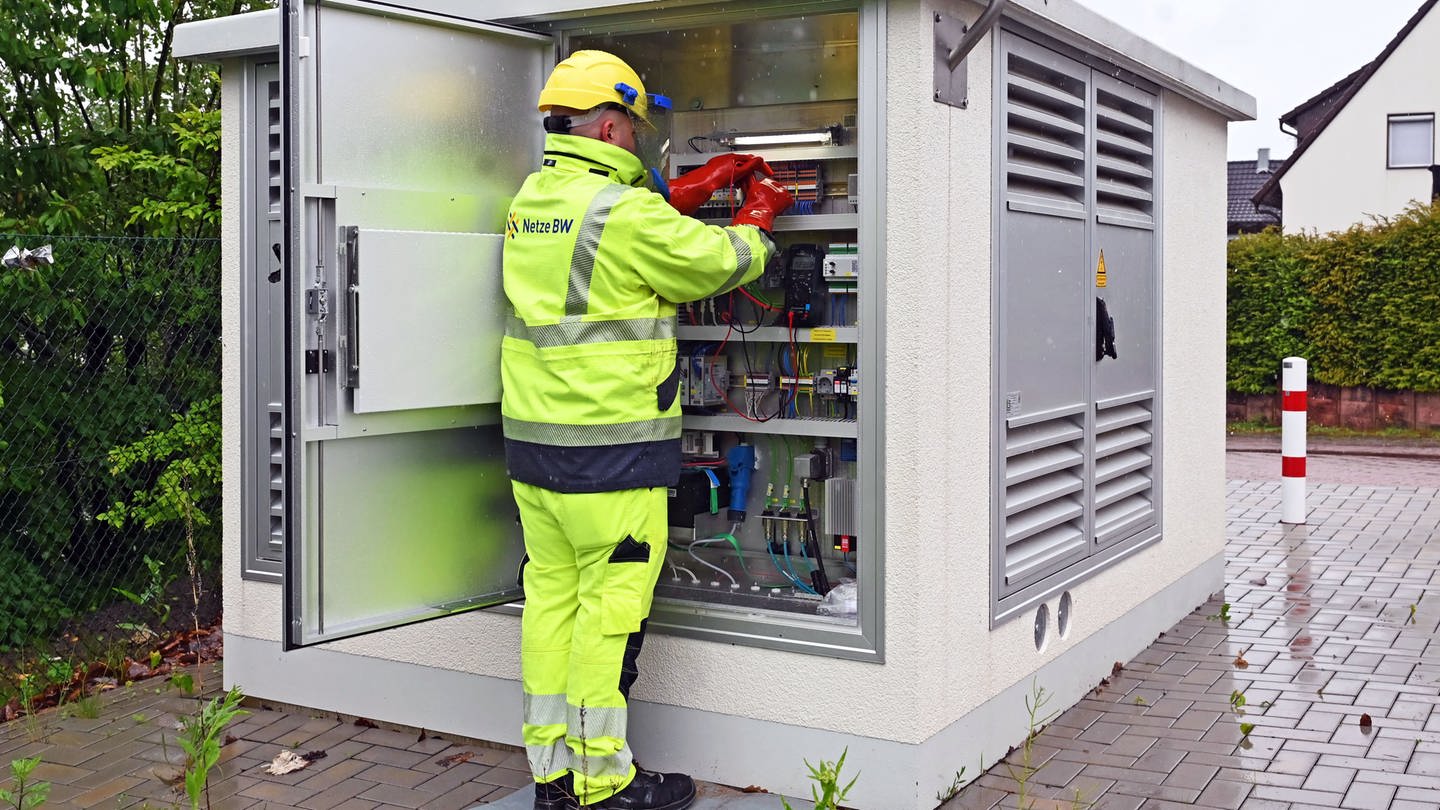 Ein Techniker vor einer Umspannstation arbeitet an Kabeln.