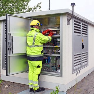 Ein Techniker vor einer Umspannstation arbeitet an Kabeln.