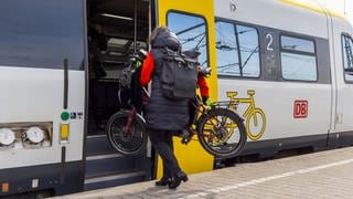 Frau steigt mit Fahrrad in Zug. In vollen Zügen kann es Ärger um die für Räder reservierten Plätze geben.