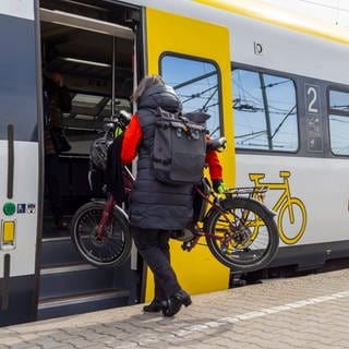 Frau steigt mit Fahrrad in Zug. In vollen Zügen kann es Ärger um die für Räder reservierten Plätze geben.