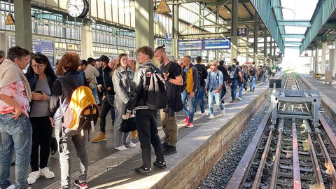 Menschen stehen im Stuttgarter Hauptbahnhof am Gleis und warten, weil ihre Züge sich verspäten oder ausfallen. 