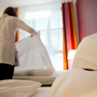 Eine Frau bezieht in einem Hotelzimmer das Bett neu.