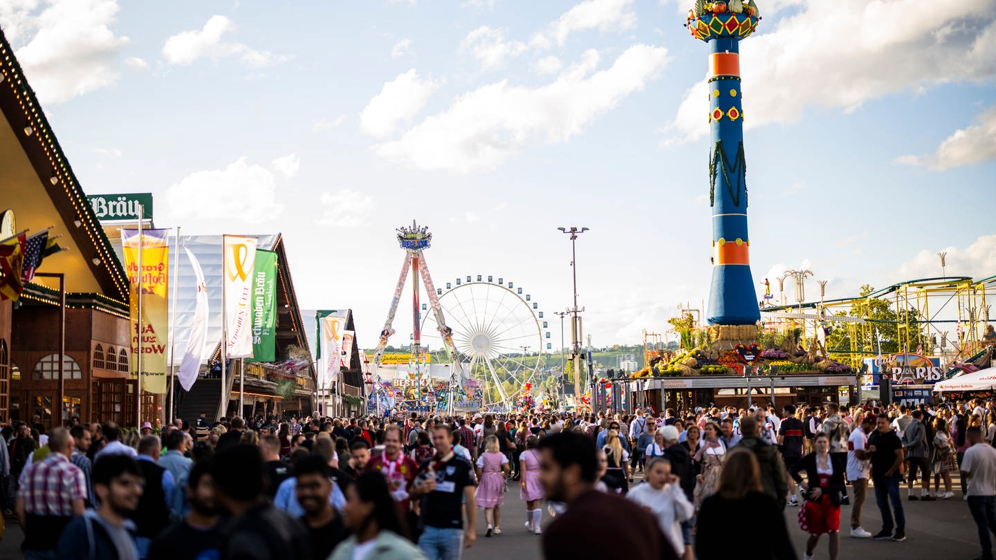 Besucherinnen und Besucher des Cannstatter Wasens 2023. Im Hintergrund das Riesenrad und die Fruchtsäule.