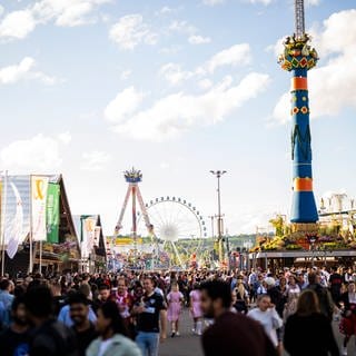 Besucherinnen und Besucher des Cannstatter Wasens 2023. Im Hintergrund das Riesenrad und die Fruchtsäule.