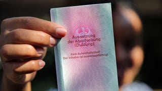 Eine Frau hält einen Ausweis für Geflüchtete in der Hand mit dem Titel: Aussetzung der Abschiebung (Duldung).