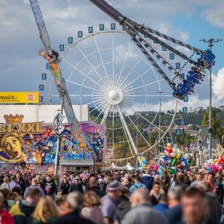 Besucher des 177. Cannstatter Volksfests gehen über den Cannstatter Wasen.