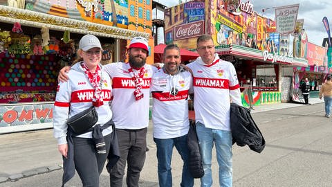 Vier VfB-Fans mit Fußball-Trikots auf dem Festgelände des Cannstatter Wasens.