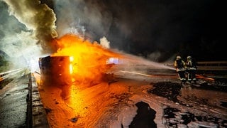 Feuerwehrleute löschen im Dunkeln auf der Autobahn einen brennenden Lkw.