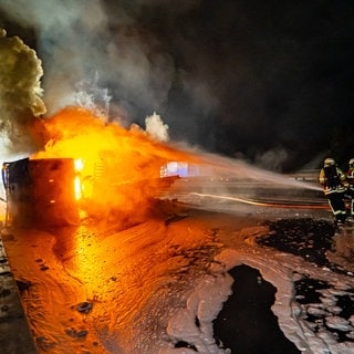 Feuerwehrleute löschen im Dunkeln auf der Autobahn einen brennenden Lkw.