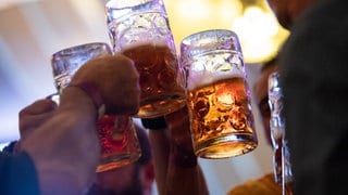 Besucher stoßen in einem Festzelt auf dem Cannstatter Volksfest mit Bierkrügen an (Archivbild).