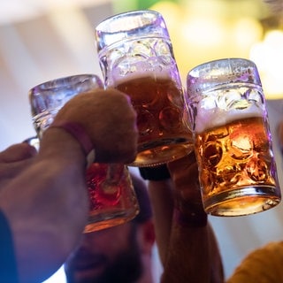 Besucher stoßen in einem Festzelt auf dem Cannstatter Volksfest mit Bierkrügen an (Archivbild).