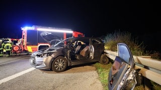 Auf der A8 bei Kirchheim unter Teck in Fahrtrichtung Stuttgart steht ein zerbeultes Auto. Ein Rad ist under der Leitplanke eingeklemmt. Die herausgerissene Fahrertür steht an der selben Leitplanke. Dahinter arbeiten Einsatzkräfte der Feuerwehr.