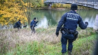 Mehrere Einsatzkräfte der Polizei durchkämmen das hohe Gras am Neckarufer.