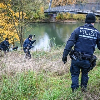 Mehrere Einsatzkräfte der Polizei durchkämmen das hohe Gras am Neckarufer.