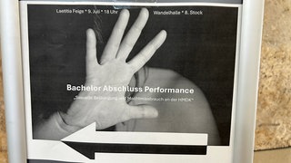 Ein graues Plakat mit der Aufschrift "Bachelor-Abschluss-Performance - Sexuelle Belästigung und Machtmissbrauch an der HMDK".