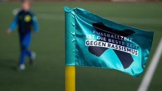 Symboldbild mit Fußballer und einer Flagge. Darauf steht: Fußballzeit ist die beste Zeit gegen Rassismus. Bei einem Fußballspiel in der Kreisklasse B zwischen dem KSC Sindelfingen und dem SV Magstadt soll am Wochenende ein Sindelfinger Spieler einen Magstadter rassistisch beleidigt haben.