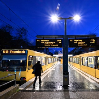 Eine Person geht in der Morgendämmerung an einer Stadtbahnhaltestelle zu einer Stadtbahn (Symbolfoto). 