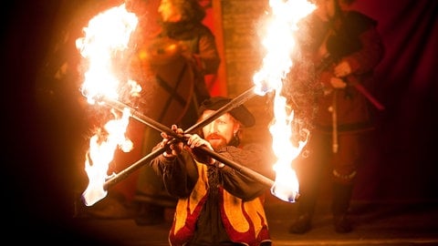 Ein mittelalterlich gekleideter Akrobat jongliert mit zwei brennenden Fackeln: Zum mittelalterlichen Weihnachtsmarkt in Esslingen gehören auch akrobatische Feuerspiele.