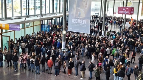 Auf dem Messegelände in Stuttgart warten viele Menschen vor den Ticketschaltern. 