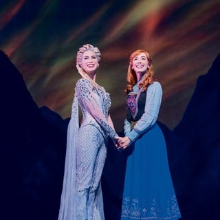 Anna und Elsa stehen im Musical "Die Eiskönigin" in Stuttgart nebeneinander auf der Bühne.