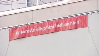 Auf einem Protestbanner, das an einem Bosch-Firmengebäude hängt, steht "Unsere Arbeitsplätze bleiben hier".