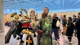 Eine verkleidete Frau und ein Mann in aufwendigen Kostümen schauen auf der Comic Con Stuttgart in die Kamera. 