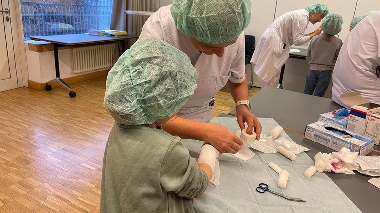 Eine Ärztin im Olgahospital in Stuttgart zeigt einer Erstklässlerin, wie man eine Wunde verbindet.